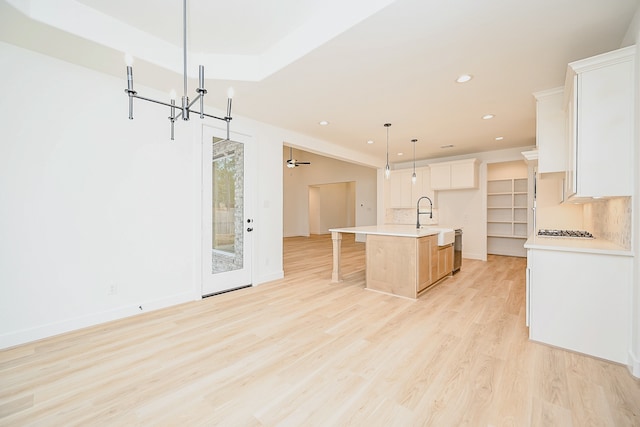 kitchen with backsplash, a kitchen island with sink, hanging light fixtures, light hardwood / wood-style floors, and white cabinetry