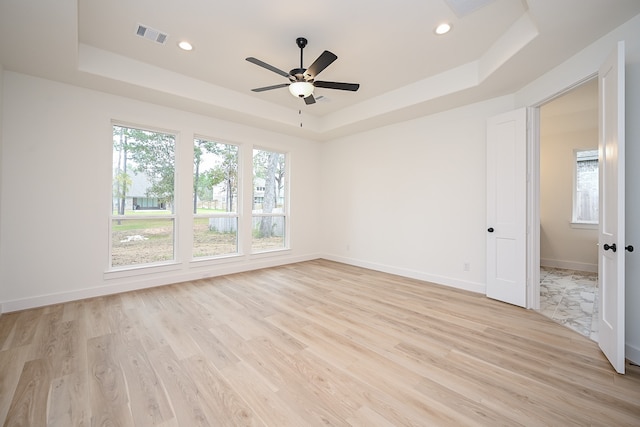 spare room with a tray ceiling, ceiling fan, and light wood-type flooring