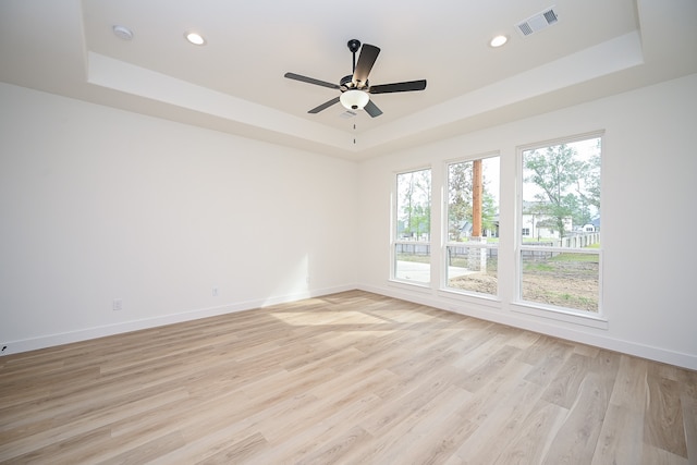 unfurnished room featuring light wood-type flooring, a tray ceiling, and ceiling fan