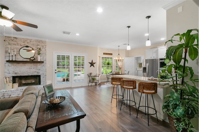 living room featuring brick wall, crown molding, a fireplace, ceiling fan with notable chandelier, and wood-type flooring