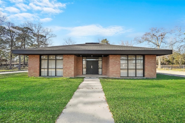 mid-century home with brick siding, a front lawn, and a shingled roof