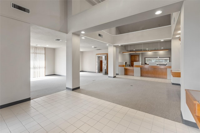 unfurnished living room featuring recessed lighting, light carpet, a high ceiling, visible vents, and baseboards