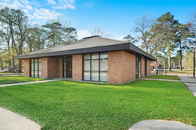 exterior space with roof with shingles, brick siding, and a front lawn