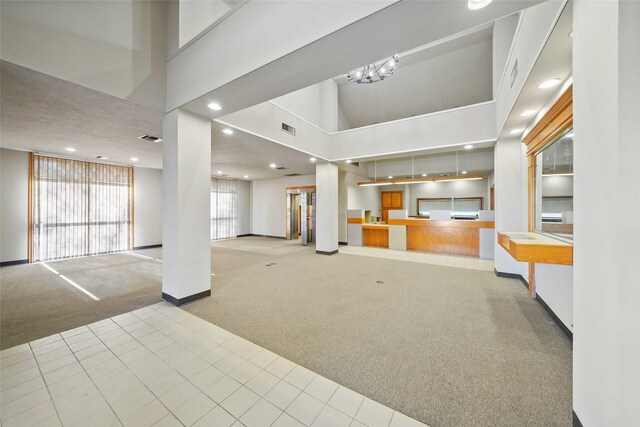 unfurnished living room featuring a high ceiling, light carpet, and a chandelier