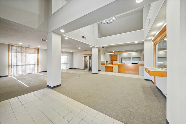 unfurnished living room with light carpet, a high ceiling, visible vents, and recessed lighting