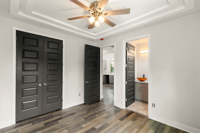 bedroom with ceiling fan, a raised ceiling, ensuite bathroom, and wood-type flooring