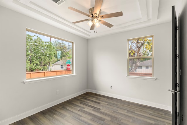 unfurnished room featuring ceiling fan, a raised ceiling, dark hardwood / wood-style floors, and a healthy amount of sunlight