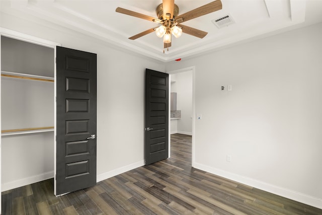 unfurnished bedroom with a tray ceiling, ceiling fan, dark wood-type flooring, and a closet