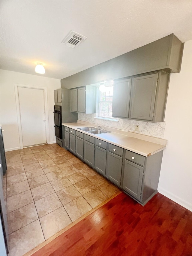 kitchen featuring visible vents, decorative backsplash, gray cabinets, light countertops, and a sink