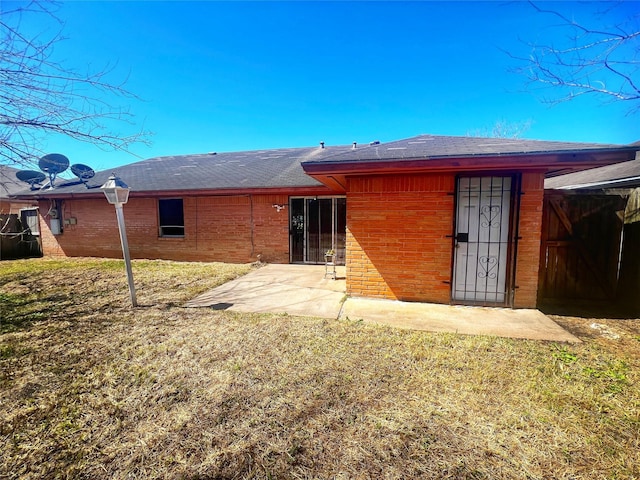 back of house featuring brick siding, a patio, and a lawn