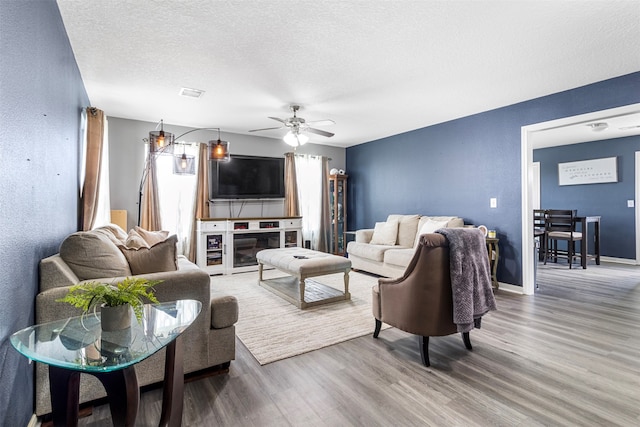 living room with hardwood / wood-style floors, ceiling fan, and a textured ceiling