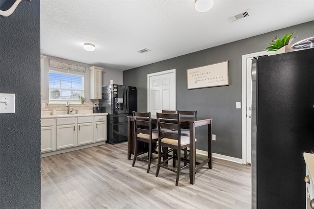 dining room featuring sink, decorative columns, a textured ceiling, and light hardwood / wood-style floors