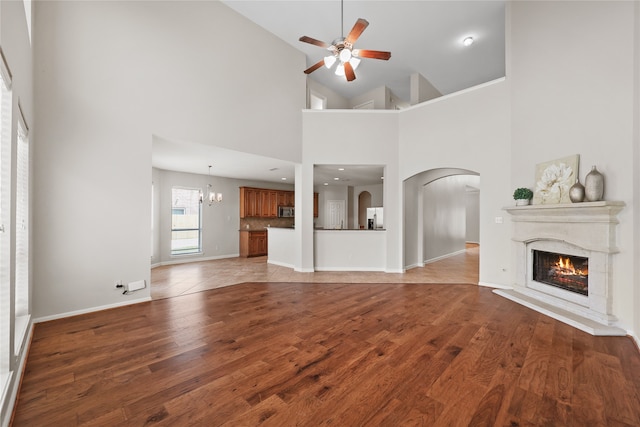 unfurnished living room with light wood-type flooring, ceiling fan with notable chandelier, and high vaulted ceiling