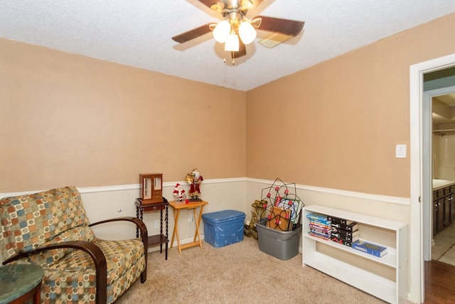 sitting room featuring ceiling fan, a textured ceiling, and light carpet