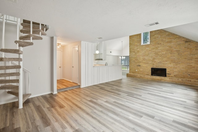 unfurnished living room with a fireplace, lofted ceiling, sink, and light hardwood / wood-style floors