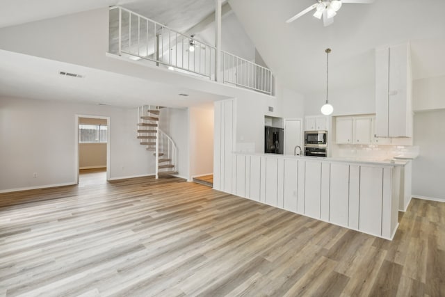 kitchen with light hardwood / wood-style flooring, white cabinetry, black fridge, high vaulted ceiling, and stainless steel microwave