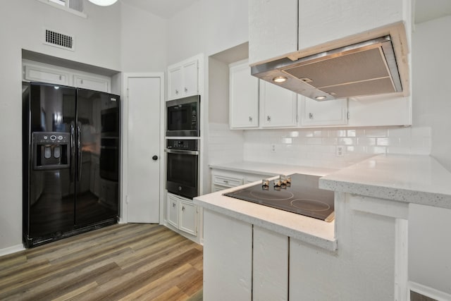 kitchen featuring black appliances, wood-type flooring, island exhaust hood, tasteful backsplash, and white cabinetry