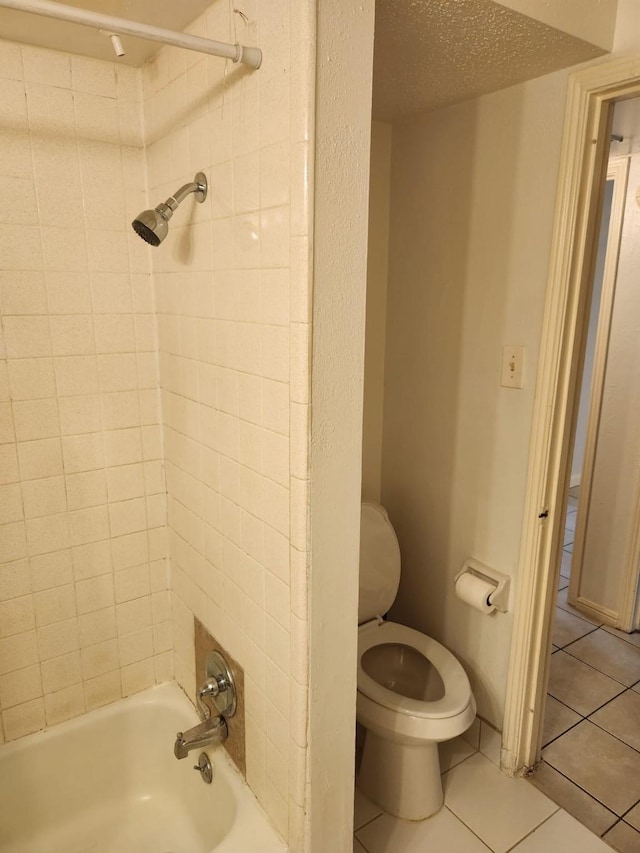 bathroom with toilet, tiled shower / bath combo, tile patterned flooring, and a textured ceiling