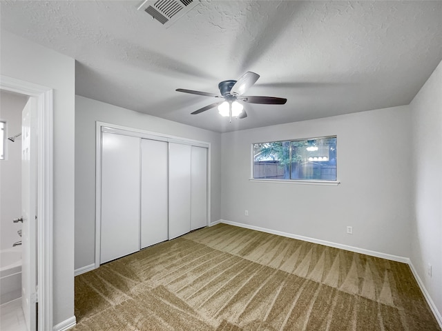 unfurnished bedroom featuring a closet, carpet floors, a textured ceiling, ensuite bathroom, and ceiling fan