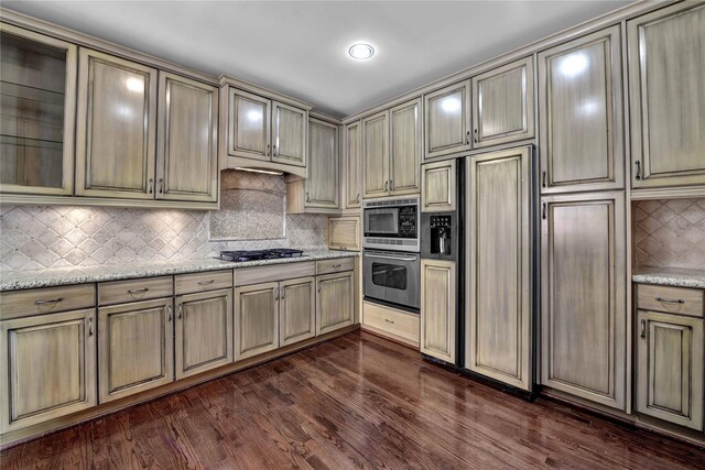 kitchen featuring dark hardwood / wood-style floors, built in appliances, decorative backsplash, and light stone countertops