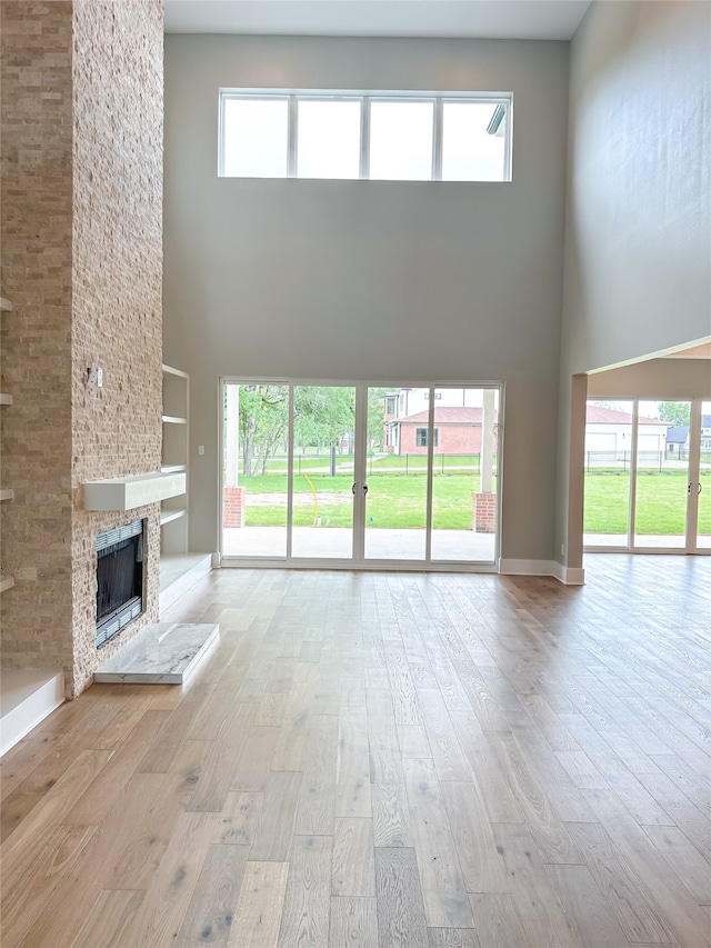 unfurnished living room featuring light wood-type flooring, a fireplace, a high ceiling, and a healthy amount of sunlight