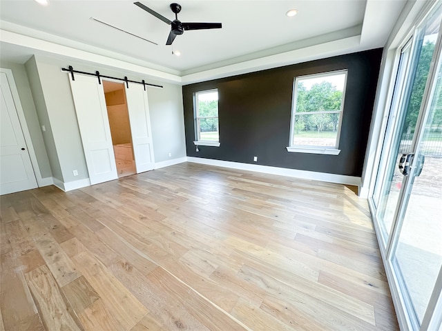 unfurnished bedroom featuring ceiling fan, a raised ceiling, light hardwood / wood-style flooring, and a barn door