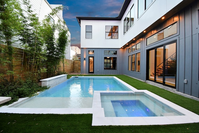 pool at dusk with a lawn and an in ground hot tub