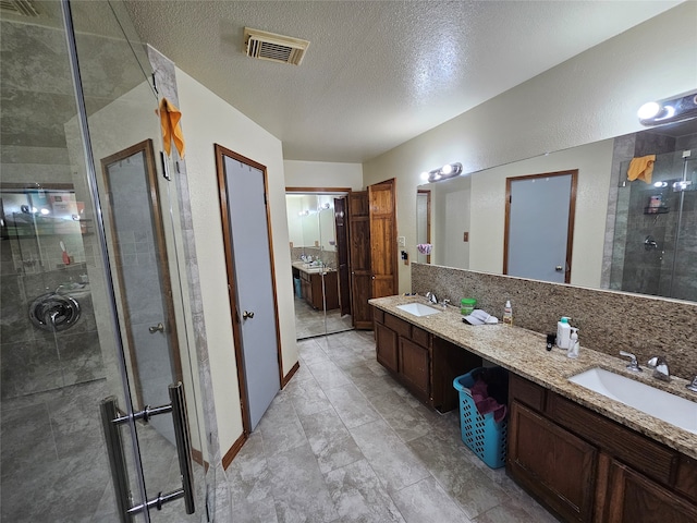 bathroom featuring tile patterned floors, a textured ceiling, a shower with shower door, and dual bowl vanity