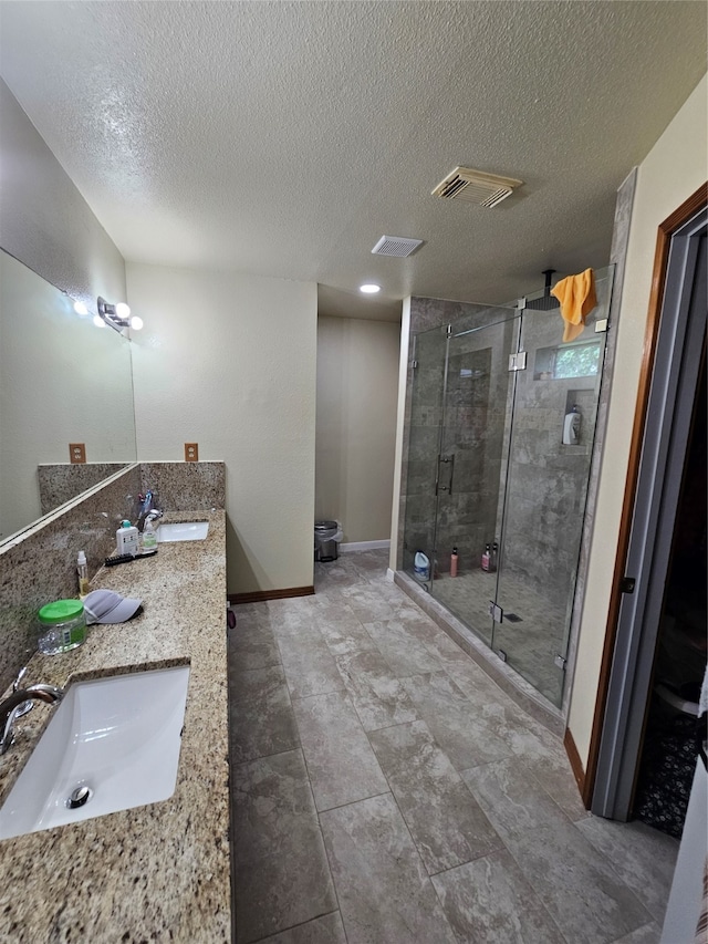 bathroom with tile patterned floors, double vanity, a shower with door, and a textured ceiling