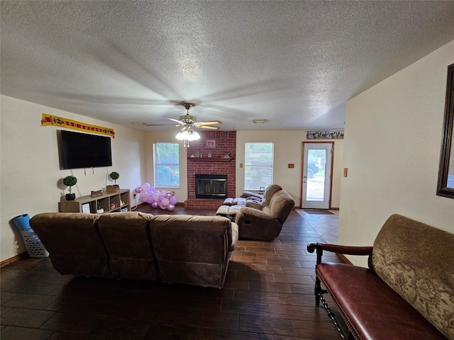 living room with a brick fireplace, dark wood-type flooring, a textured ceiling, ceiling fan, and brick wall