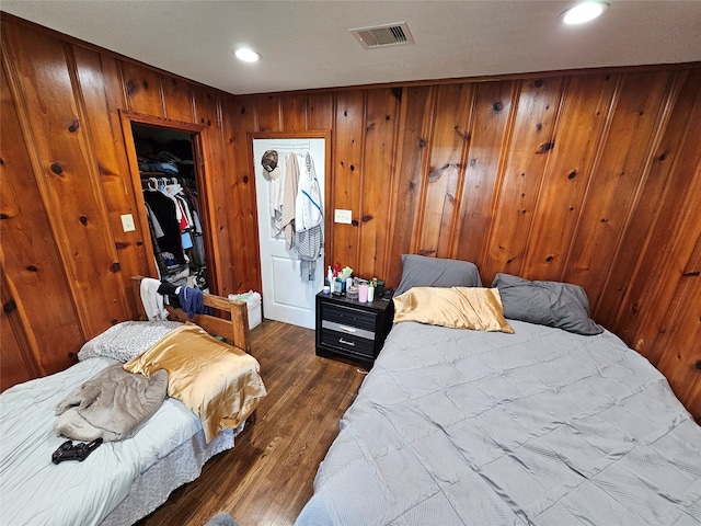 bedroom featuring dark hardwood / wood-style flooring, wooden walls, and a closet