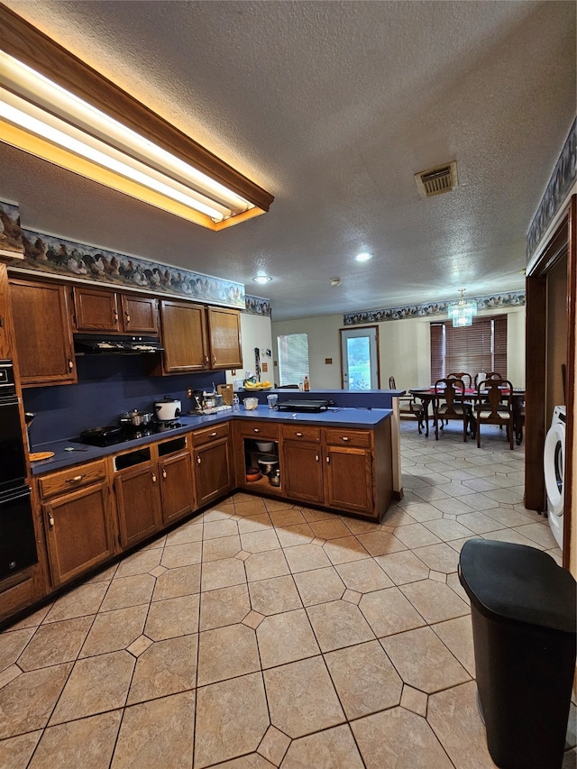 kitchen with washer / dryer, kitchen peninsula, black electric cooktop, multiple ovens, and a textured ceiling