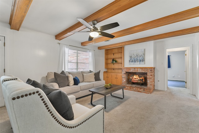 carpeted living room featuring built in shelves, ceiling fan, beamed ceiling, and a brick fireplace