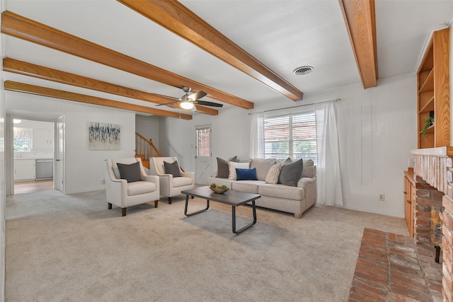 living room featuring light colored carpet, ceiling fan, a brick fireplace, and beam ceiling