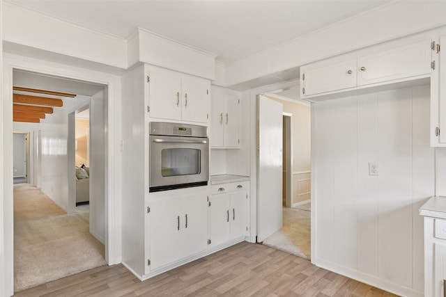 kitchen featuring beamed ceiling, crown molding, white cabinetry, oven, and light hardwood / wood-style floors