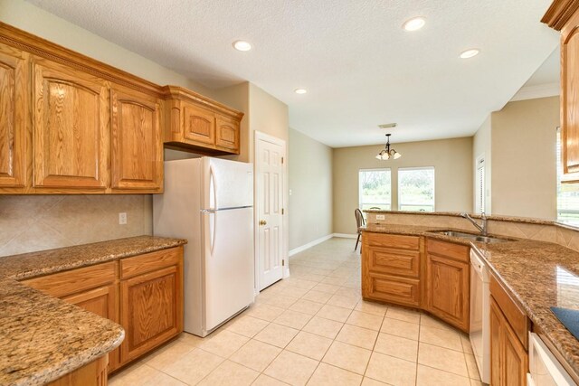 kitchen with hanging light fixtures, light tile patterned floors, sink, stone counters, and white appliances