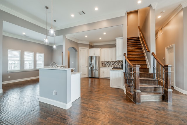 kitchen with backsplash, stainless steel refrigerator with ice dispenser, hanging light fixtures, white cabinets, and a center island with sink