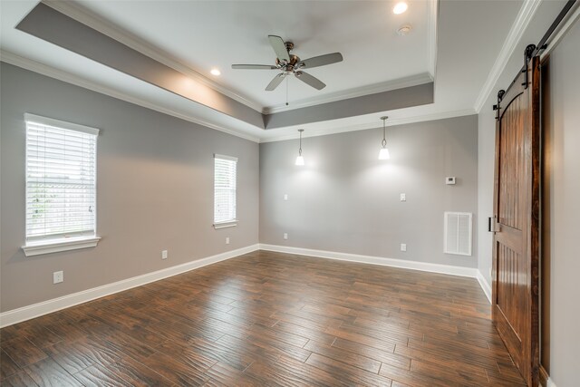 empty room with crown molding, dark hardwood / wood-style flooring, a barn door, a tray ceiling, and ceiling fan