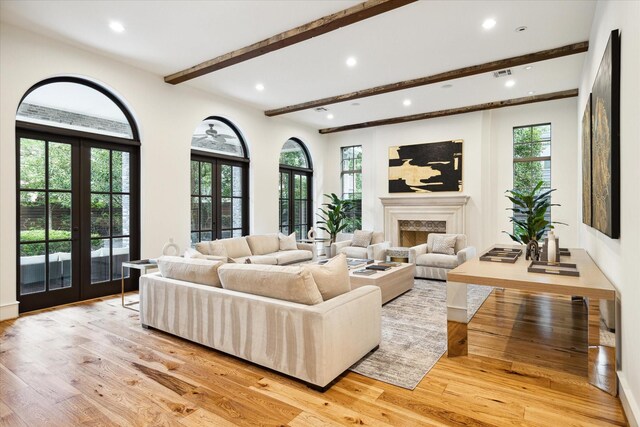 living room with light wood-type flooring, french doors, a high end fireplace, and beamed ceiling