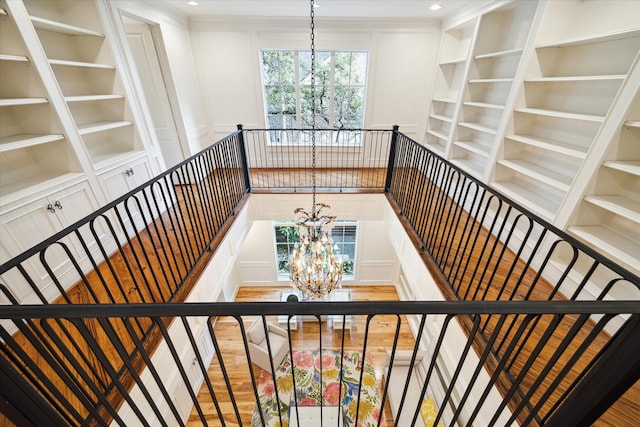 stairway with built in features, a chandelier, crown molding, and wood-type flooring