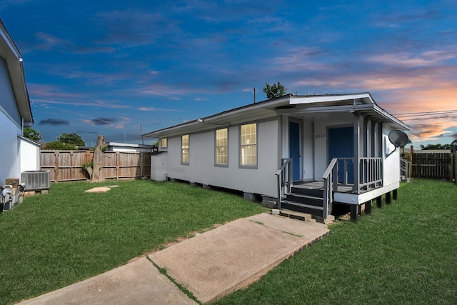 back house at dusk featuring a yard and cooling unit