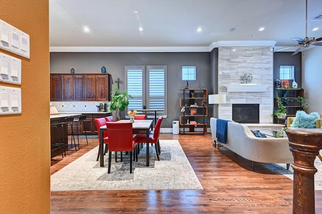 dining room with a large fireplace, ornamental molding, a wealth of natural light, and wood finished floors