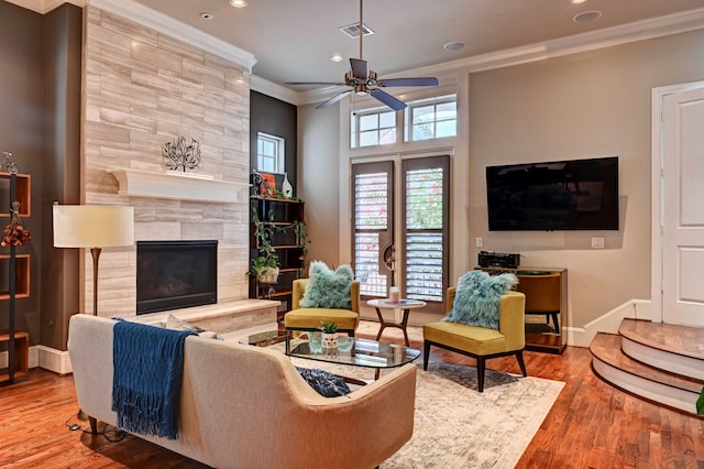 living room featuring ceiling fan, hardwood / wood-style flooring, ornamental molding, and a tile fireplace