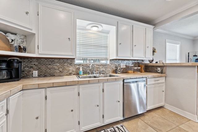 kitchen with tile countertops, a sink, white cabinets, stainless steel dishwasher, and tasteful backsplash