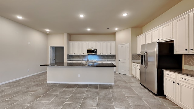 kitchen featuring a kitchen island with sink, a sink, white cabinets, appliances with stainless steel finishes, and dark stone countertops