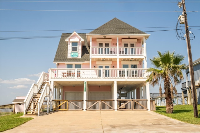 raised beach house with a shingled roof, concrete driveway, and an attached garage