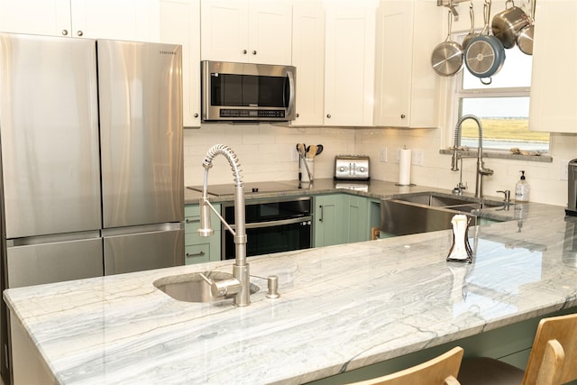 kitchen with stainless steel appliances, stone counters, a sink, and white cabinetry