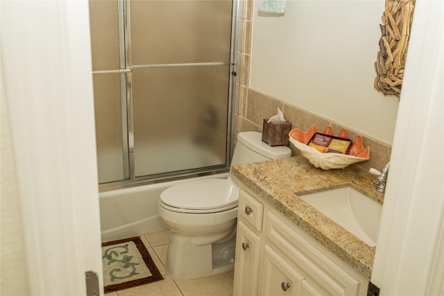 bathroom with shower / bath combination with glass door, tile walls, toilet, vanity, and tile patterned flooring