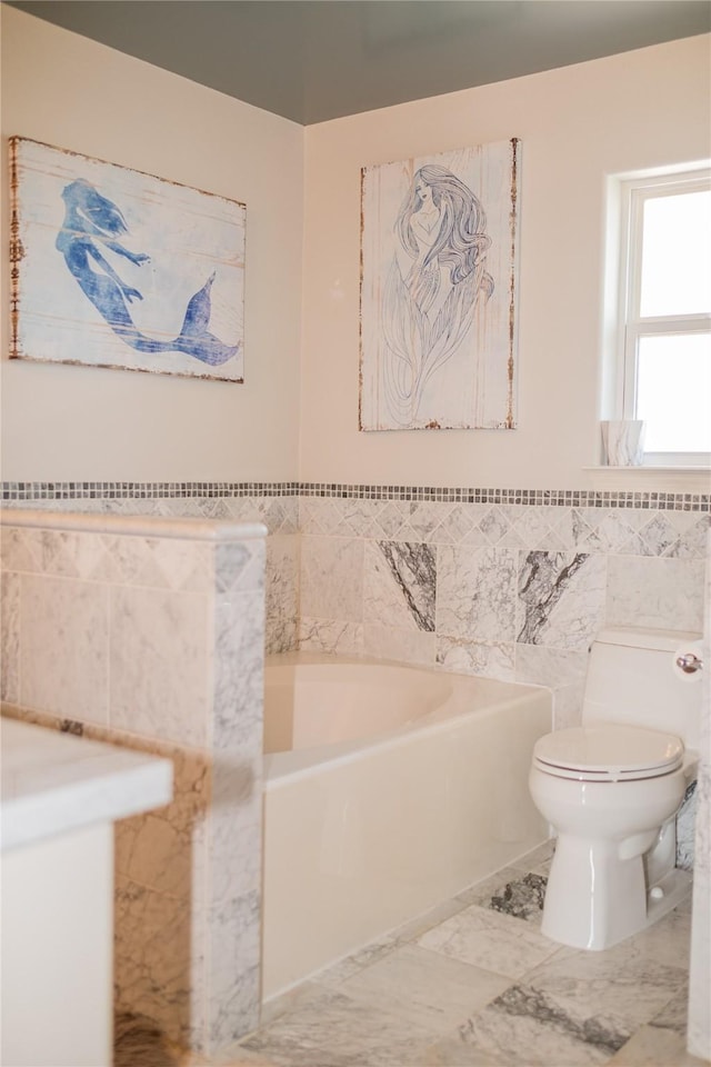 bathroom featuring toilet, a garden tub, marble finish floor, and tile walls