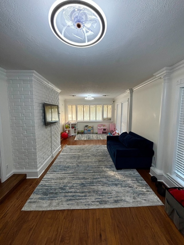 living room with dark hardwood / wood-style floors, ornamental molding, a textured ceiling, and brick wall